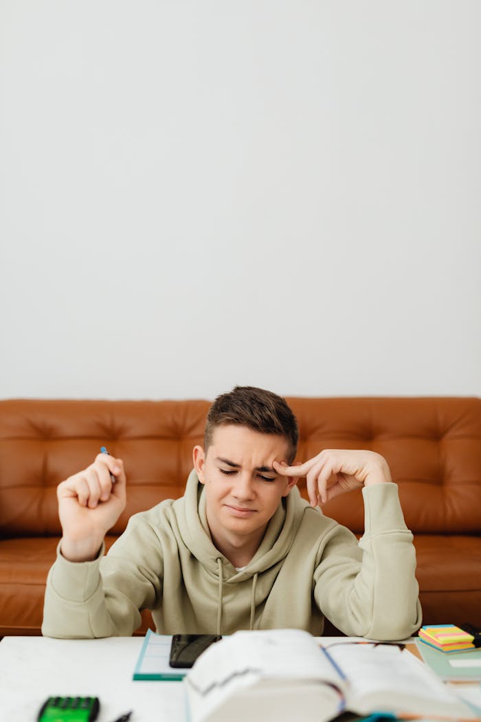 A young man intensely studying, sitting at home with materials spread on the table.